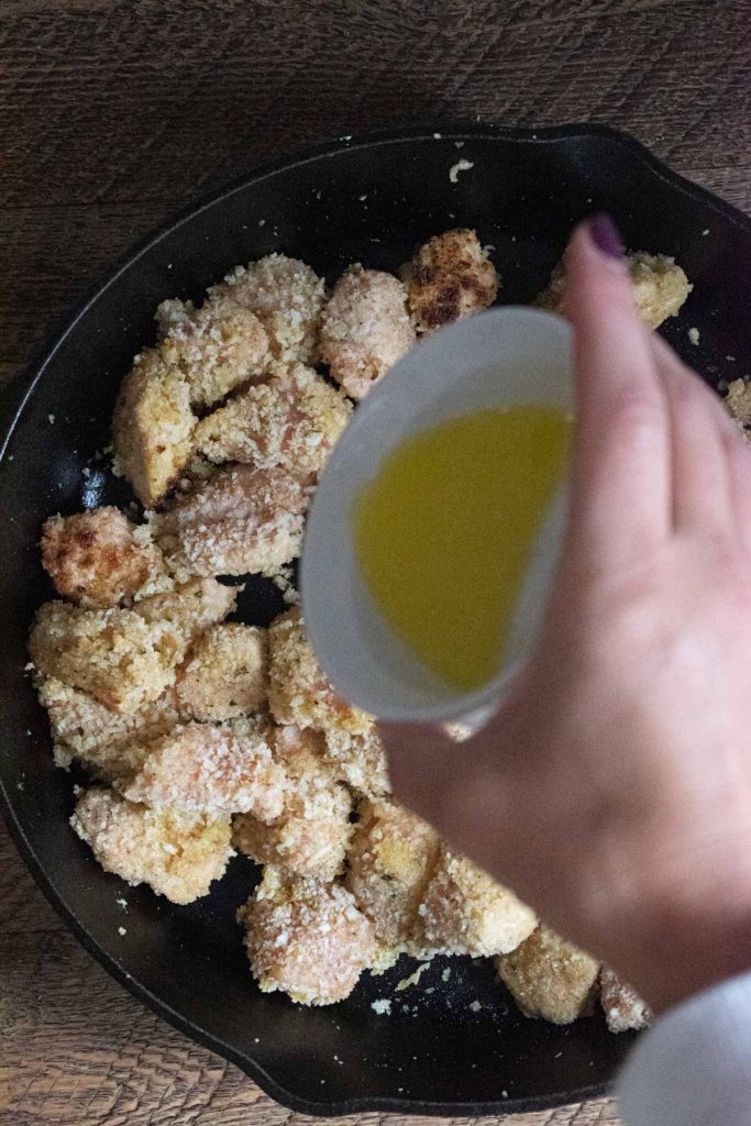 melted butter being dumped on top of garlic chicken bites frying in a cast iron skillet