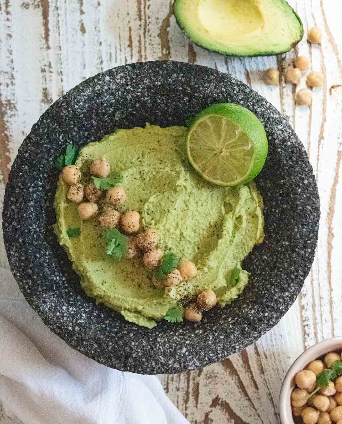 birds-eye view of avocado hummus in a black charcoal bowl with chickpeas and cilantro scattered on top