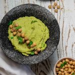 avocado hummus in a black charcoal bowl topped with scattered chickpeas and cilantro