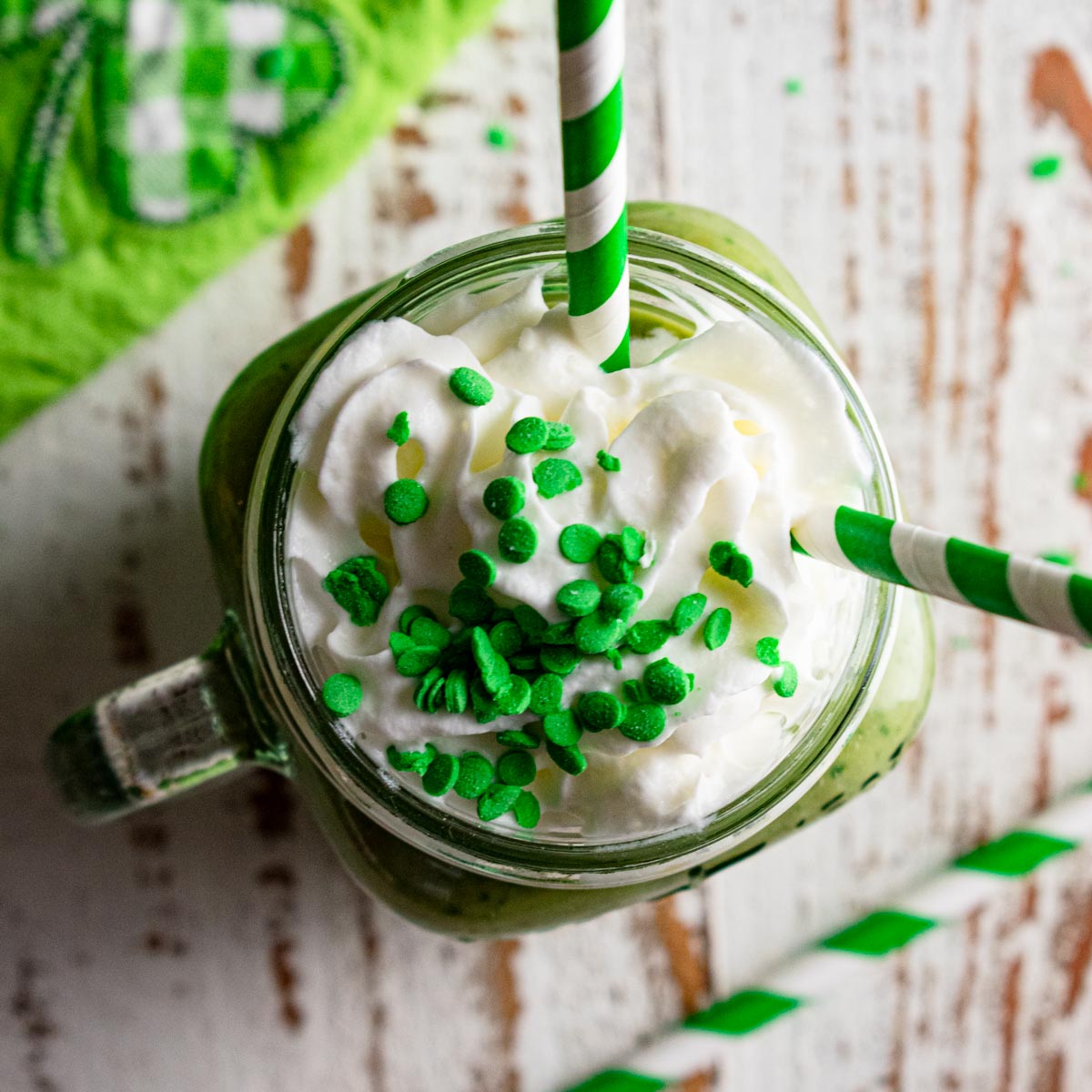 a top shot of a smoothie with whipped cream, green sprinkles, and a green and white striped straw