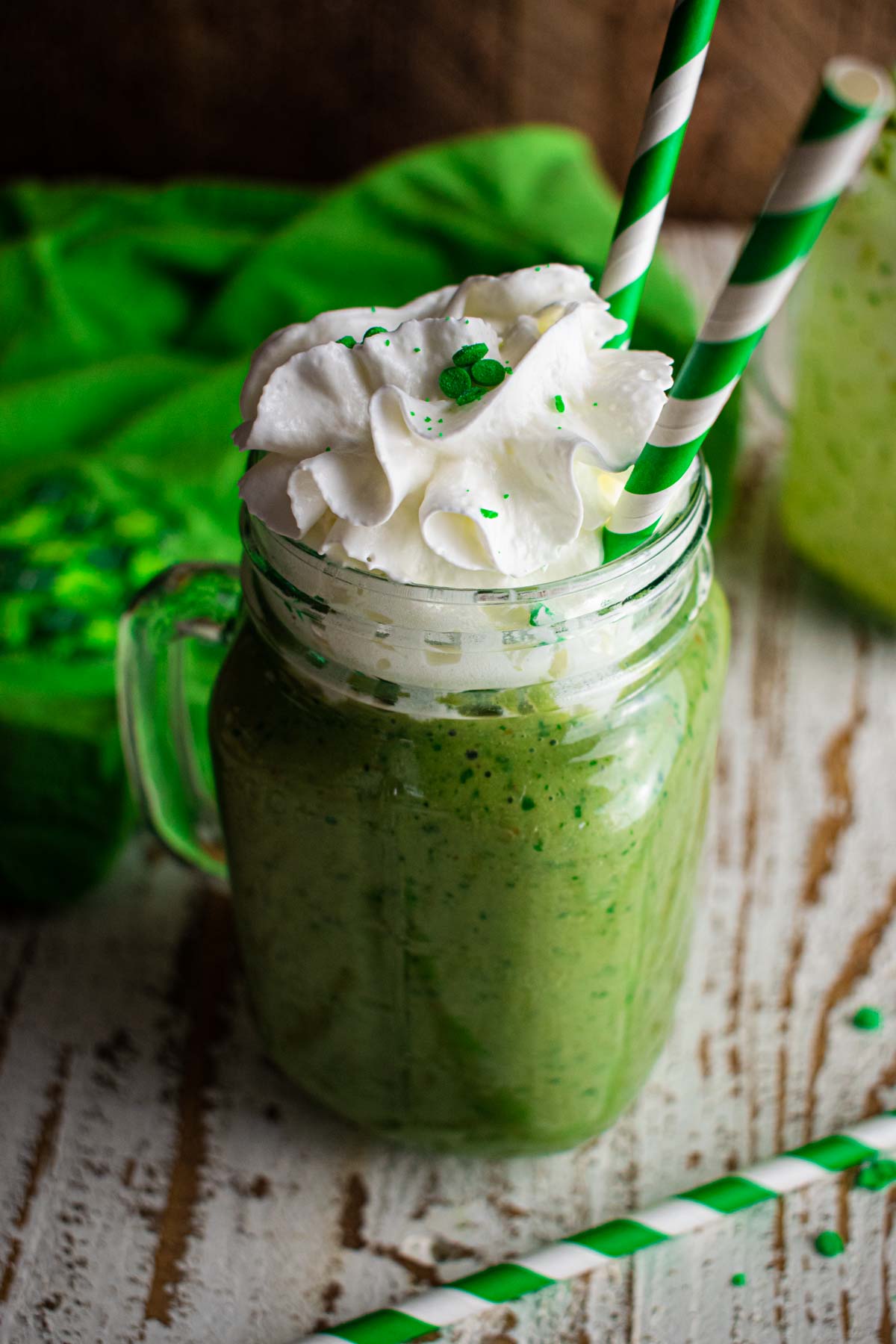 a delicious protein shamrock shake topped with whipped cream, green sprinkles, and a green and white striped straw