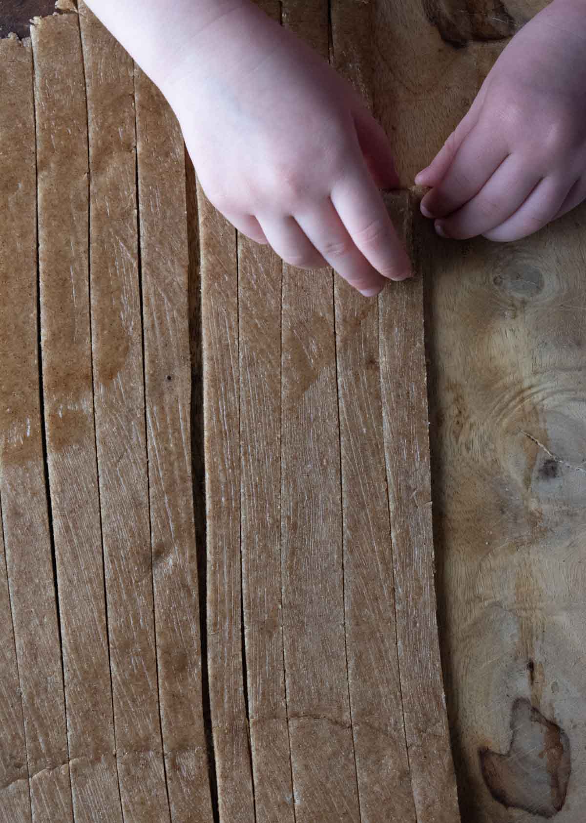 birds-eye view of a child's hand rolling strips of dough into pinwheels.