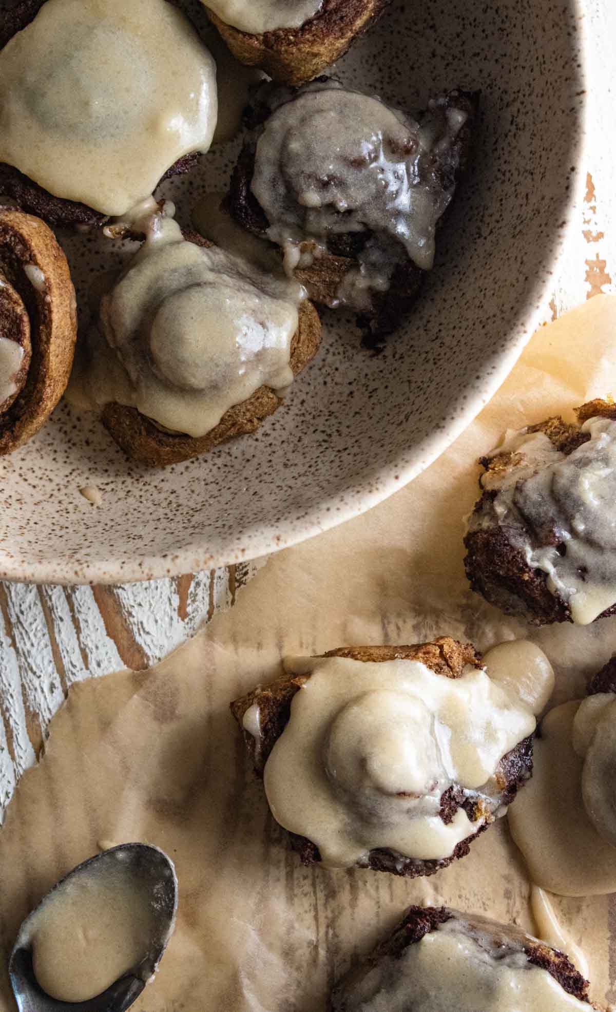 gooey, cinnamon buns topped with melted cream cheese icing on a white wooden board with cream cheese icing melting down the sides.