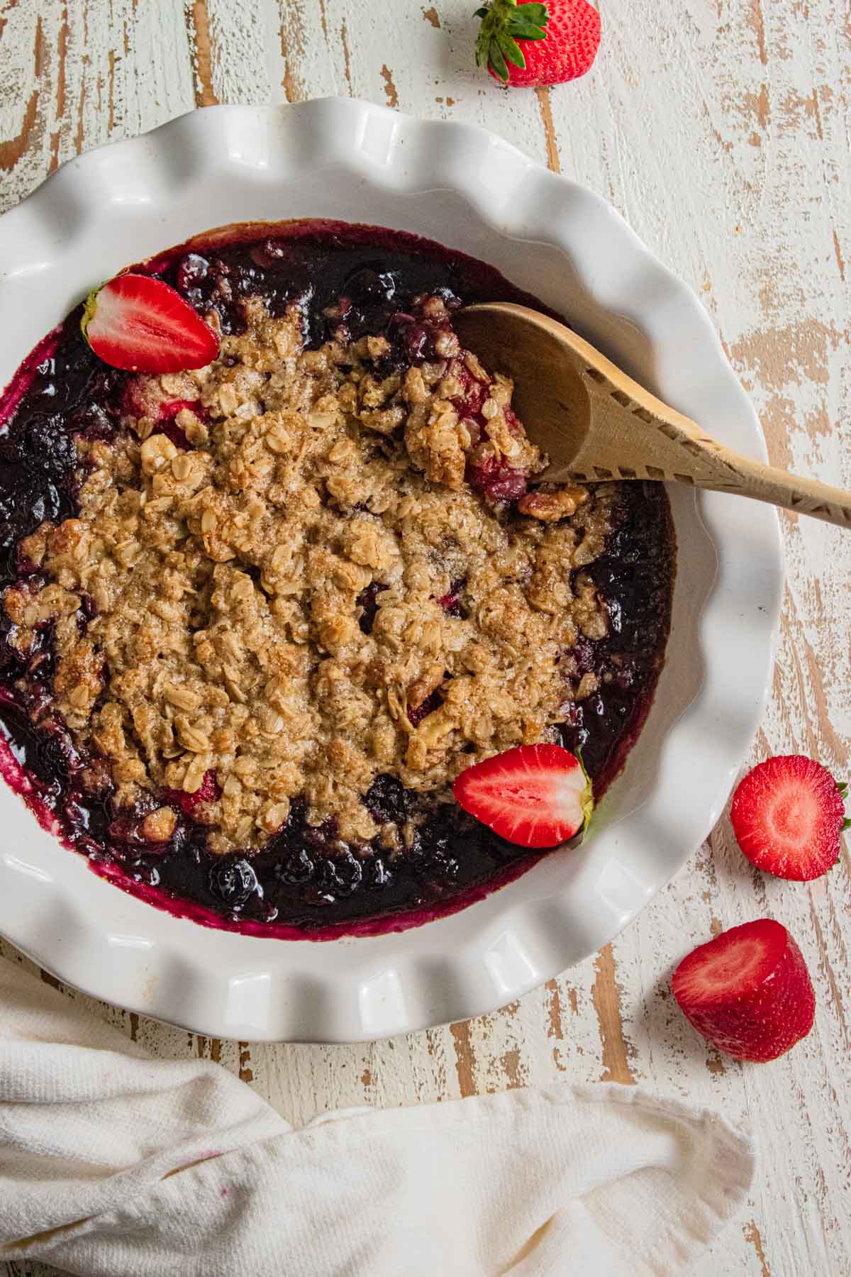 birds-eye view of a fruit crisp topped with freshly sliced strawberries and a wooden spoon slotted into the dish