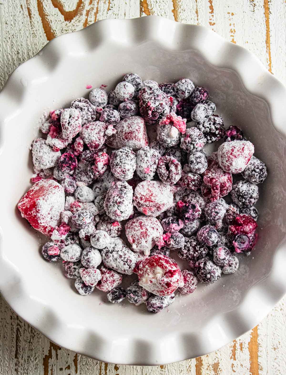 Mixed berries in a white pie dish covered with cornstarch and lemon juice. Step 1 in your cooking process.