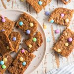 birds eye view of Easter blondies on a white plate on a white wooden board topped with mutli-colored m&ms