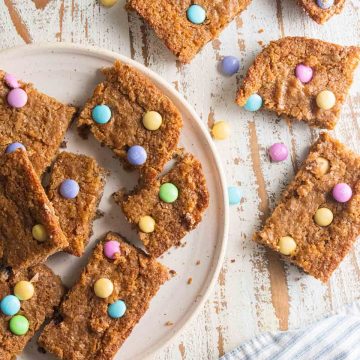 birds eye view of Easter blondies on a white plate on a white wooden board topped with mutli-colored m&ms