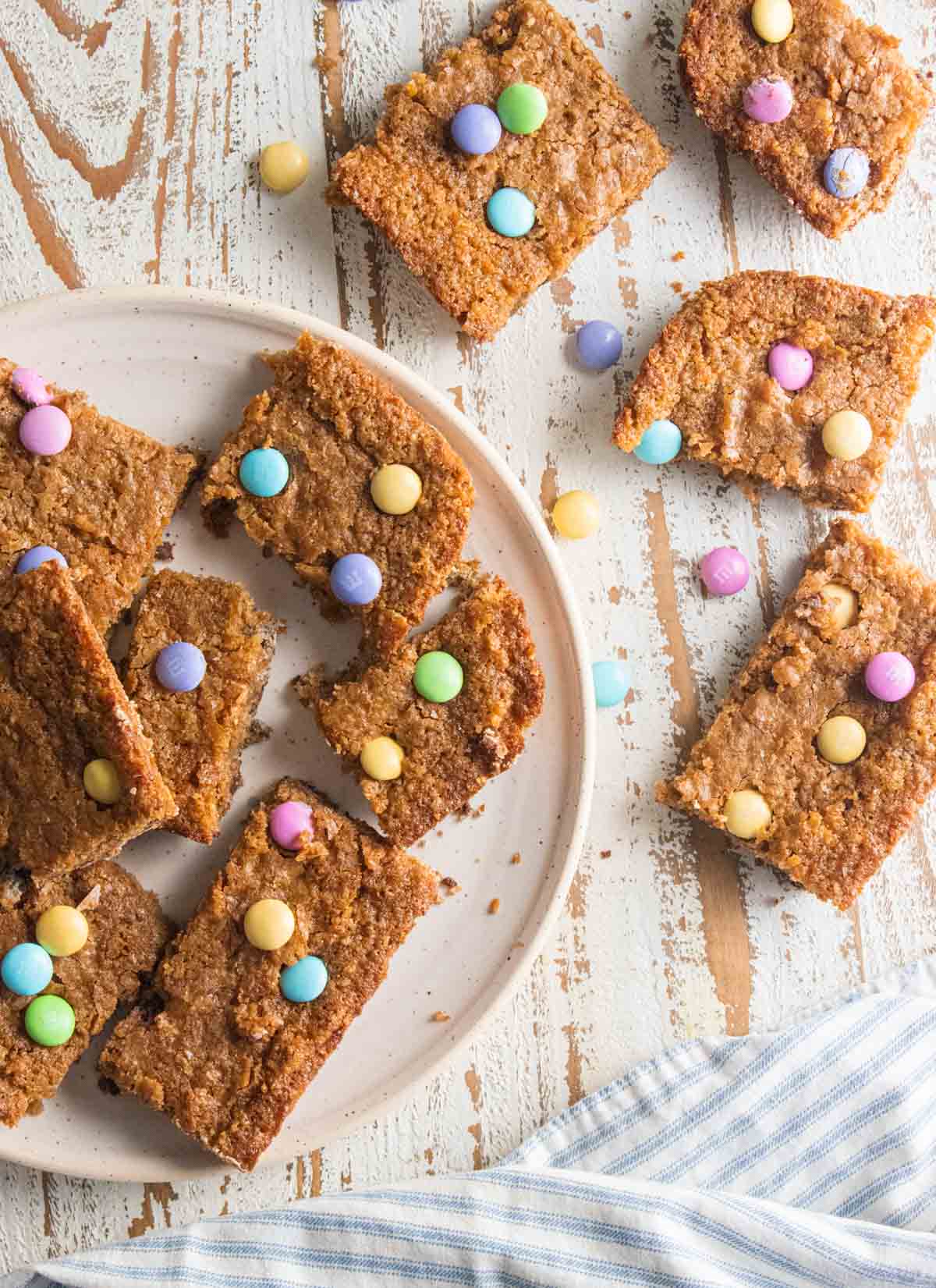 birds eye view of Easter blondies on a white plate on a white wooden board topped with mutli-colored m&ms