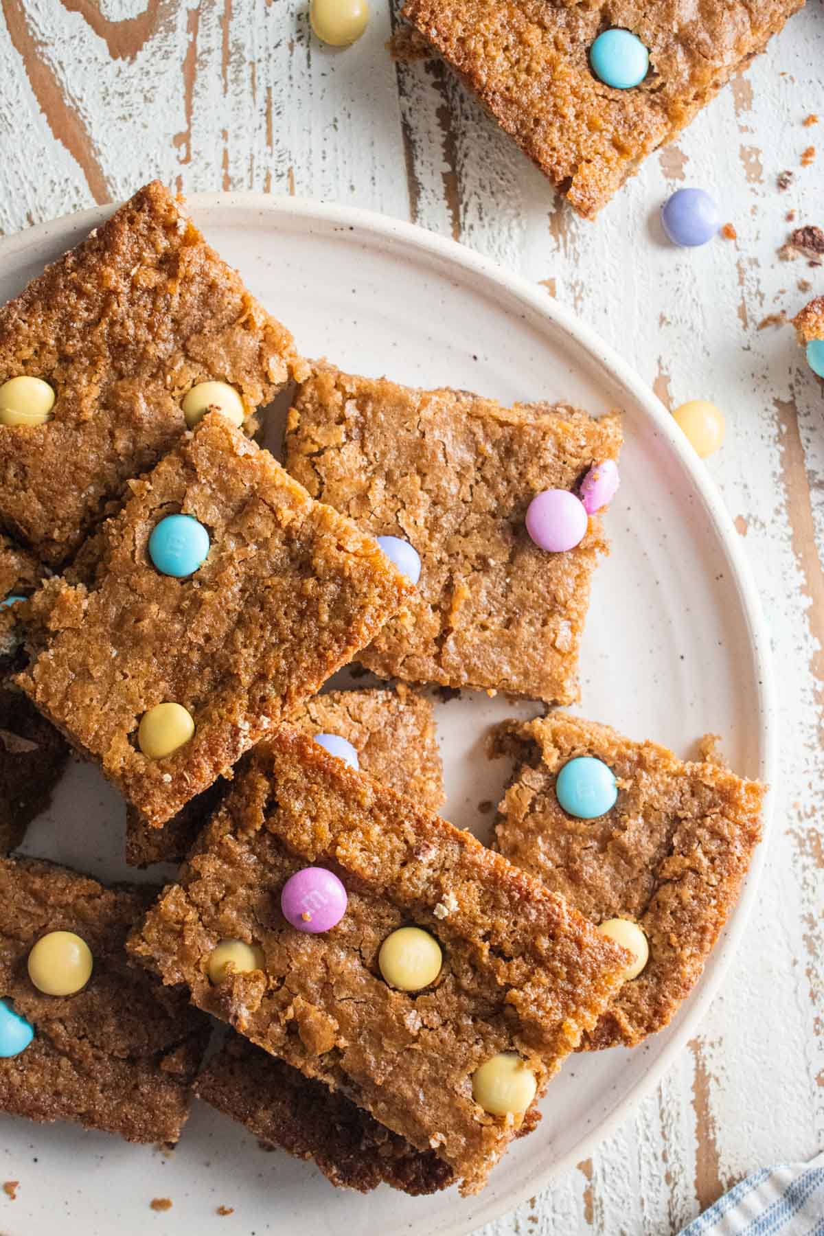 birds eye view healthy easter blondies on a white plate sitting on a white wooden board with scattered m&ms around