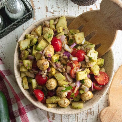 birds eye view of delicious refreshing summer salad in a tan bowl on a white wooden board with a wooden slotted spoon