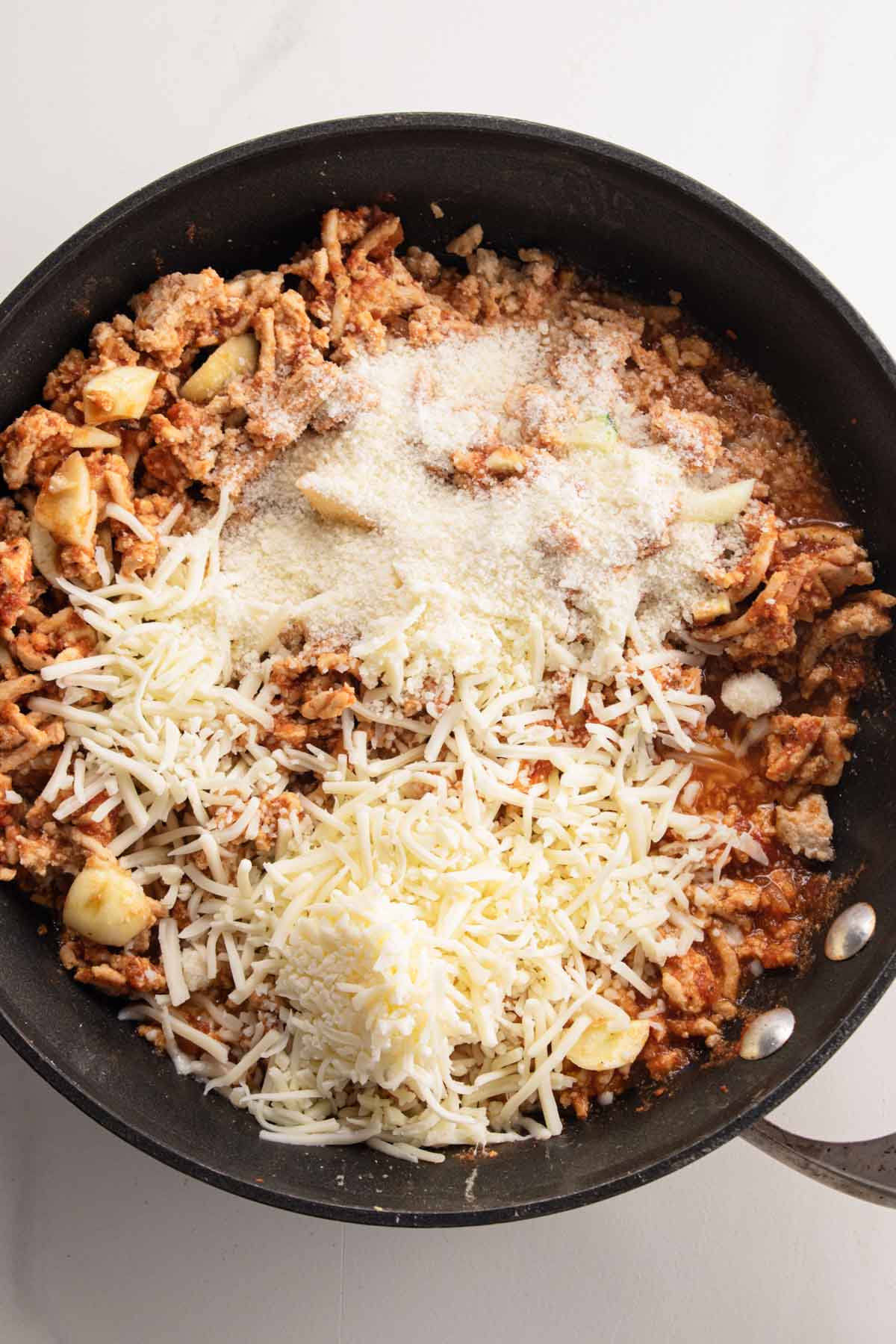 showing step 4 of the cooking process - ground chicken in a non-stick skillet topped with mozzarella and parmesan cheese. 