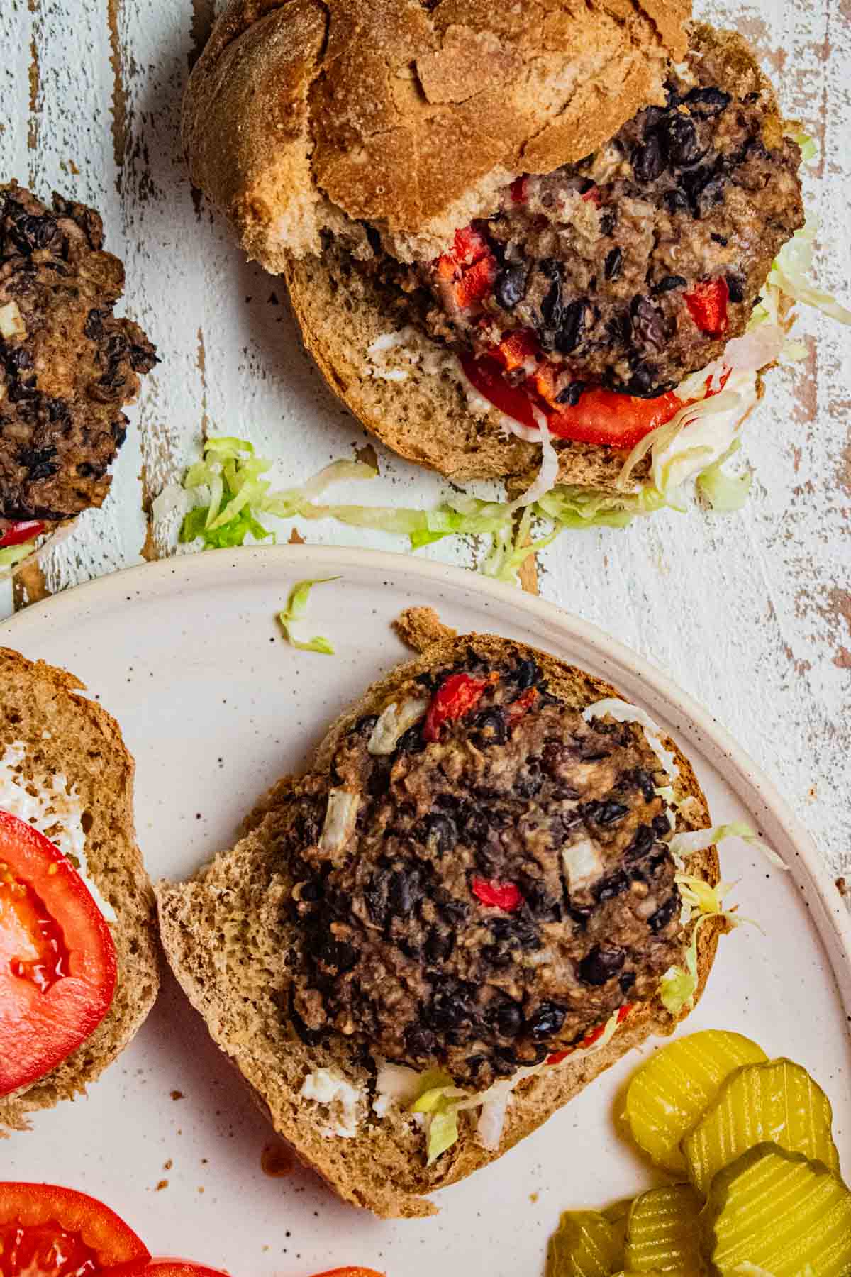 a  black bean burger on a cream colored plate with tomatoes, shredded lettuce, and a smear of mayonnaise