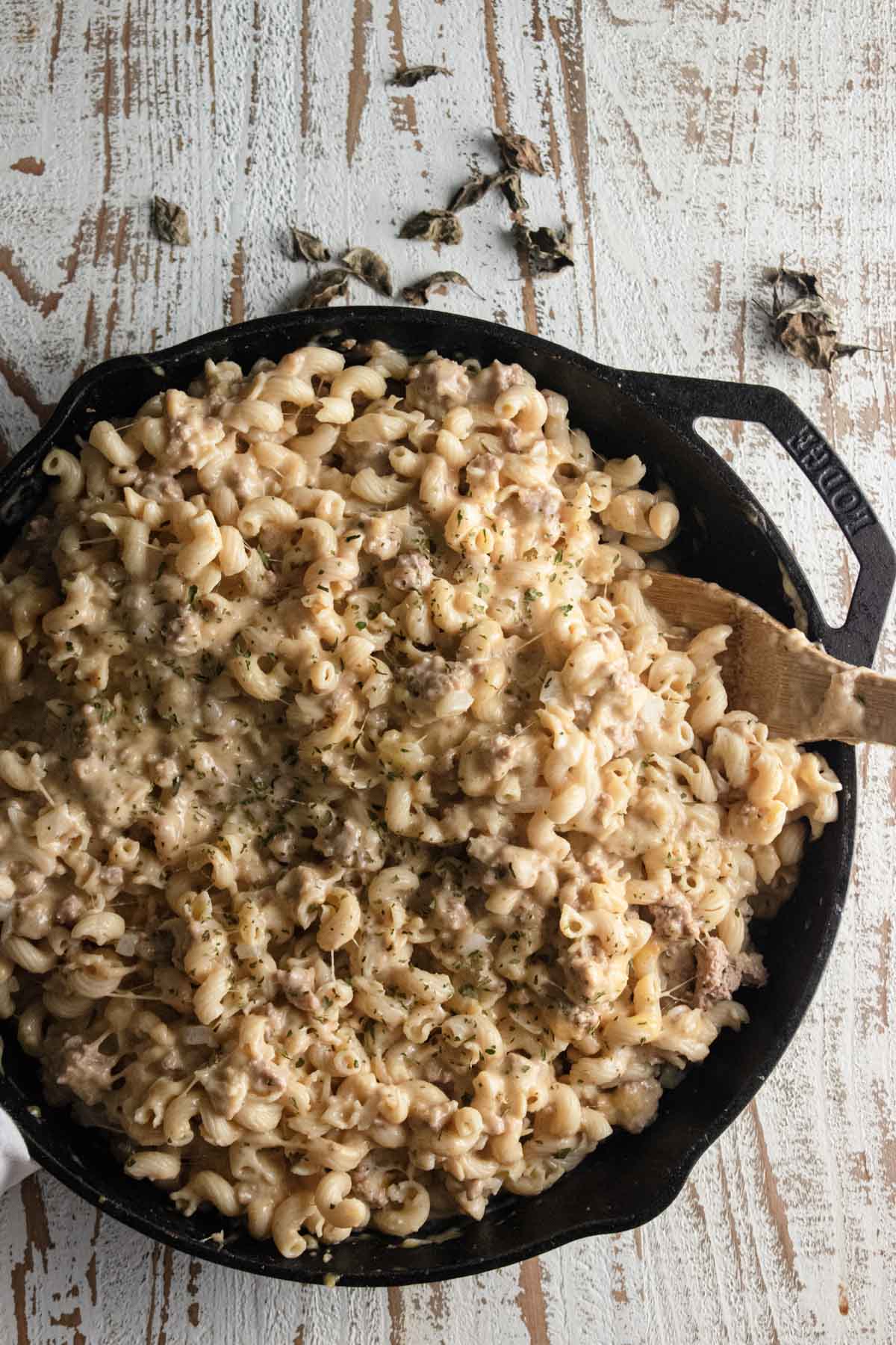 a birds-eye view of ground turkey mac and cheese in a lodge cast iron skillet with a wooden spoon slotted in the side