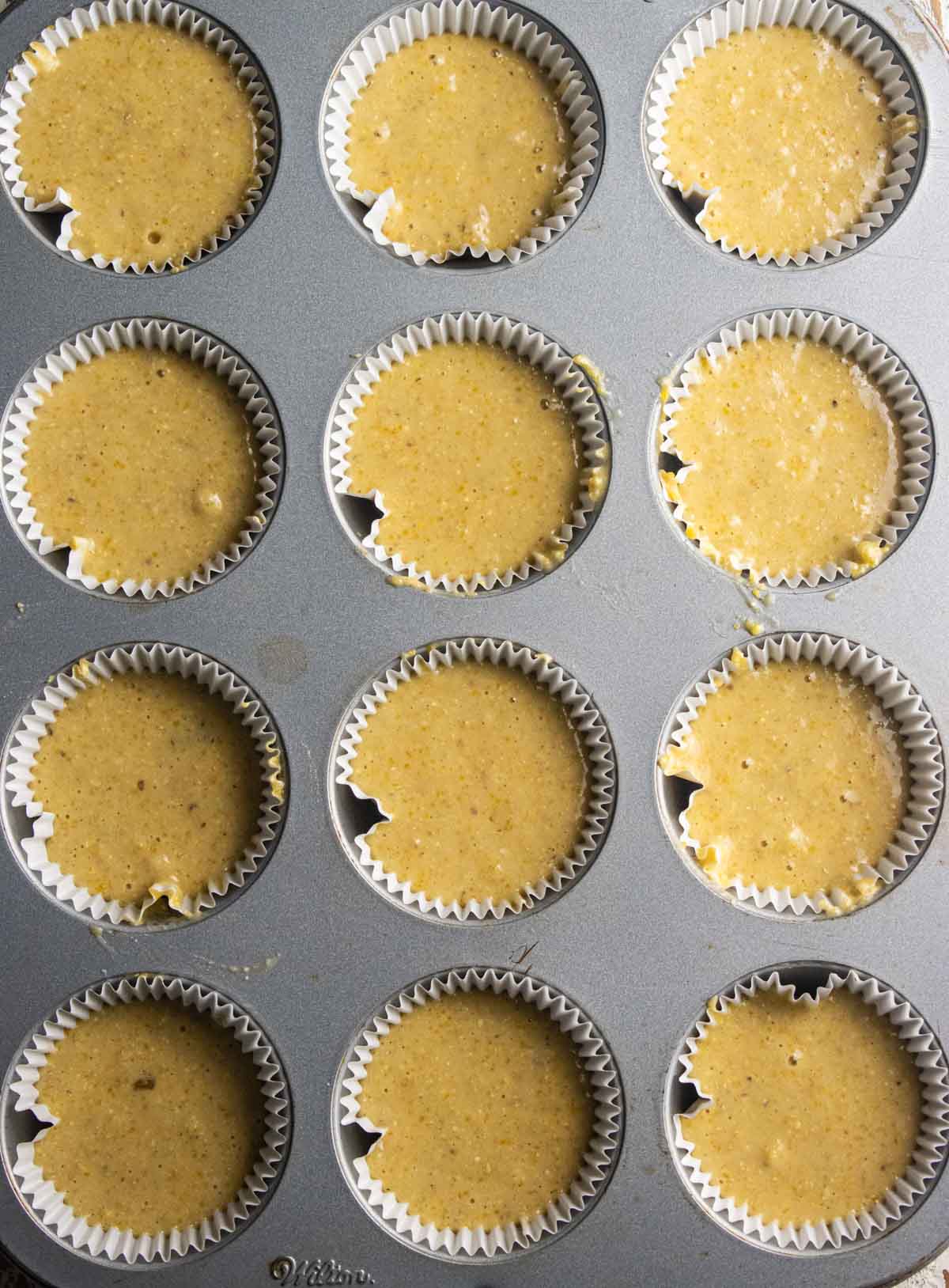 Step 5 of the baking process. A muffin tin filled with the corn  muffin mix filled halfway up each muffin cup.