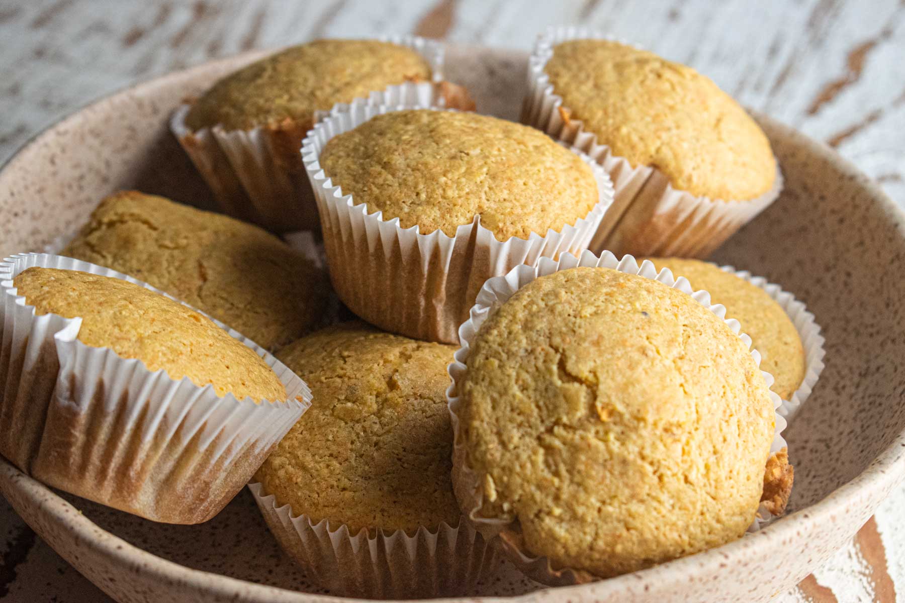 close up of the corn muffins in a cream colored bowl on a white wooden board.