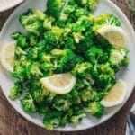 A birds-eye view of broccoli on a white plate topped with sliced lemon wedges.
