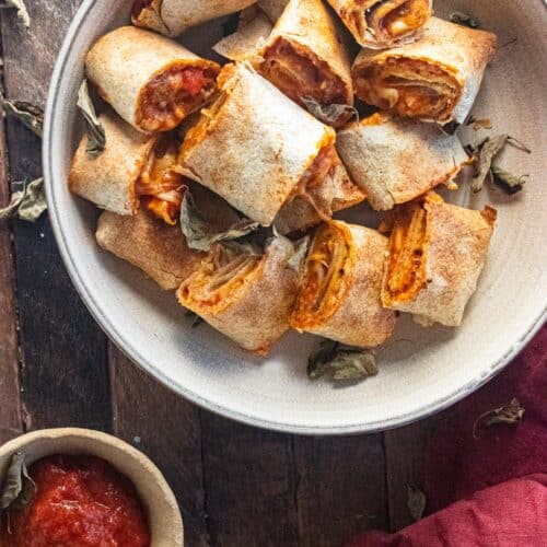 Air Fryer pizza rolls on a cream-colored plate with a side of sauce on a wooden table.