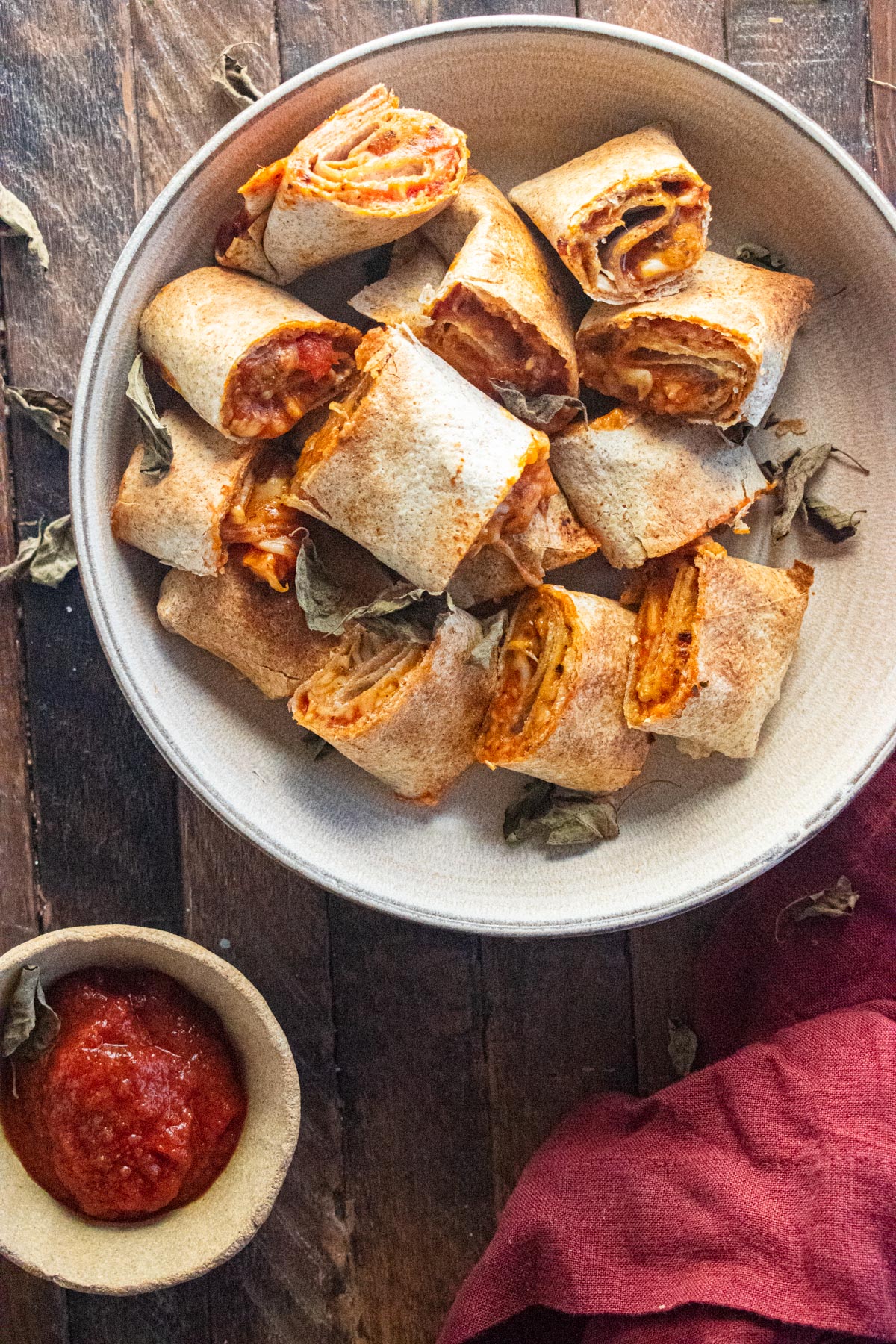 Air Fryer pizza rolls on a cream-colored plate with a side of sauce on a wooden table.