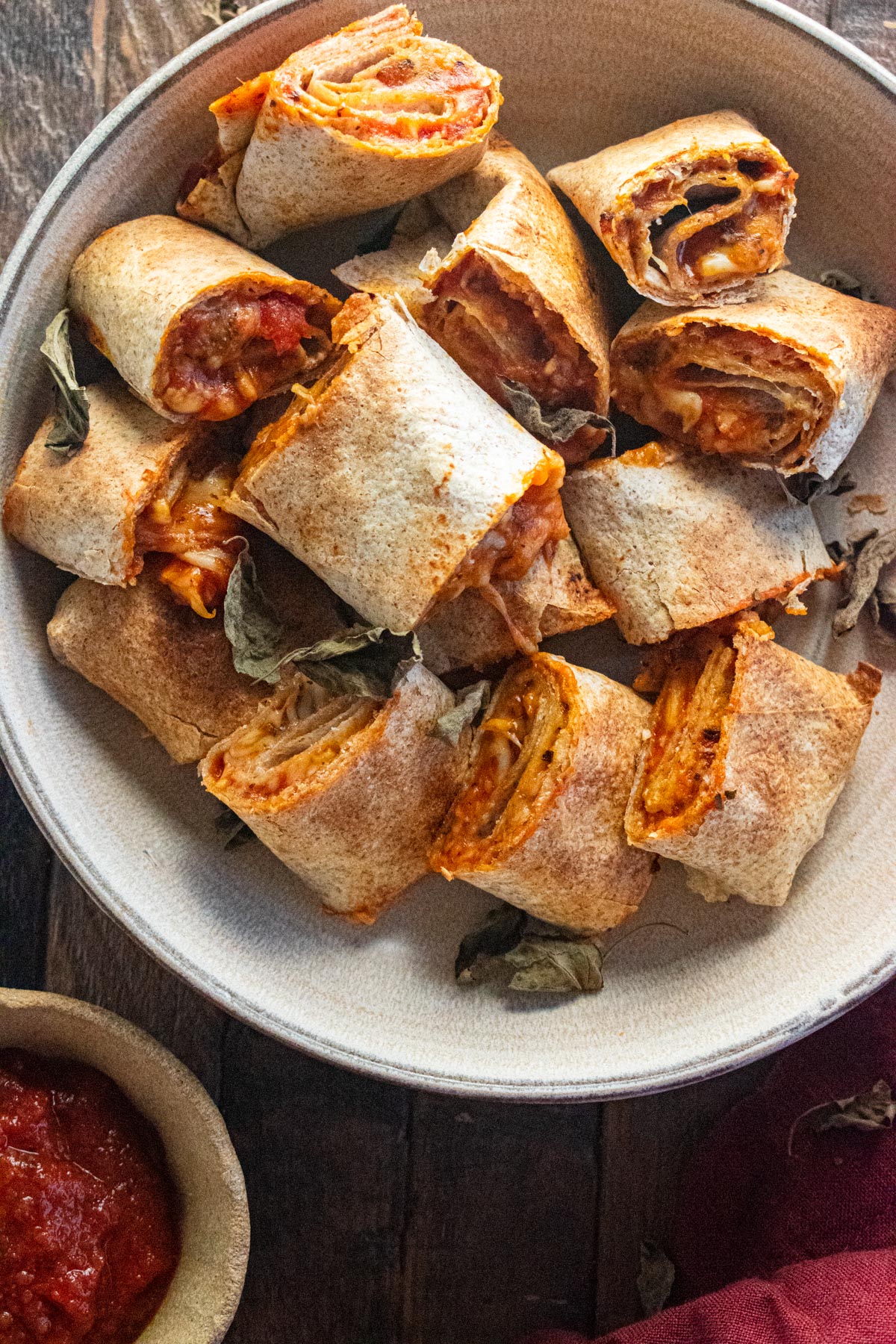 Close up of air fryer pizza rolls on a cream coloreed plate with a side of sace.