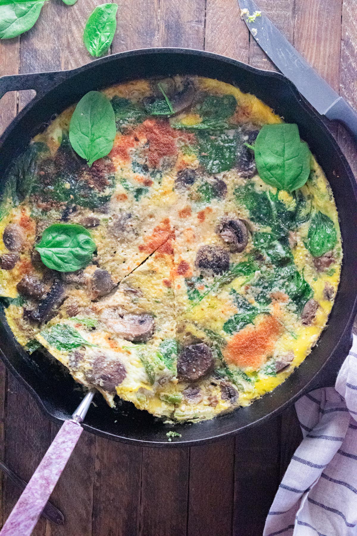 A birds-eye view of a veggie frittata in a Lodge cast-iron skillet on a wooden table with a knife laid next to the skillet.