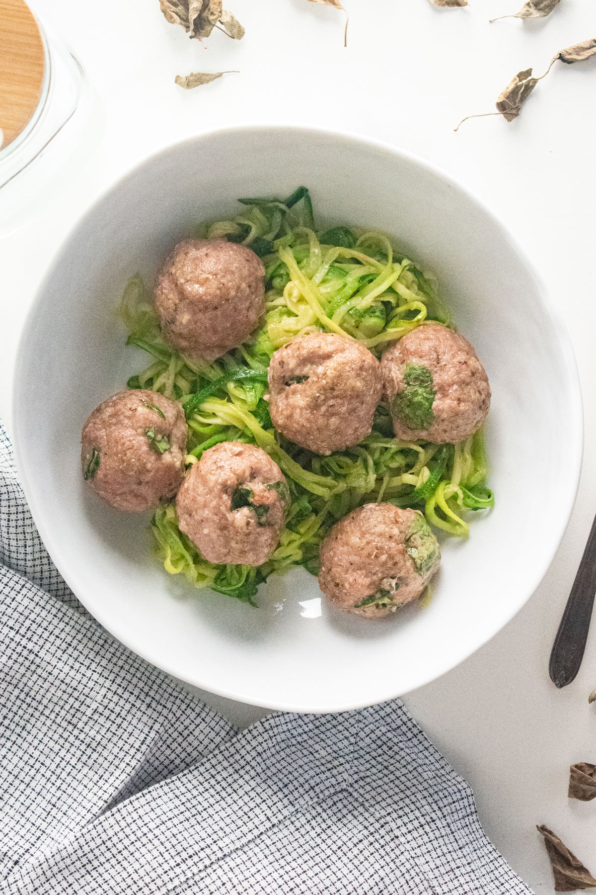 Ground turkey meatballs over zoodles in a white bowl with a checkered napkin next to the bowl. 