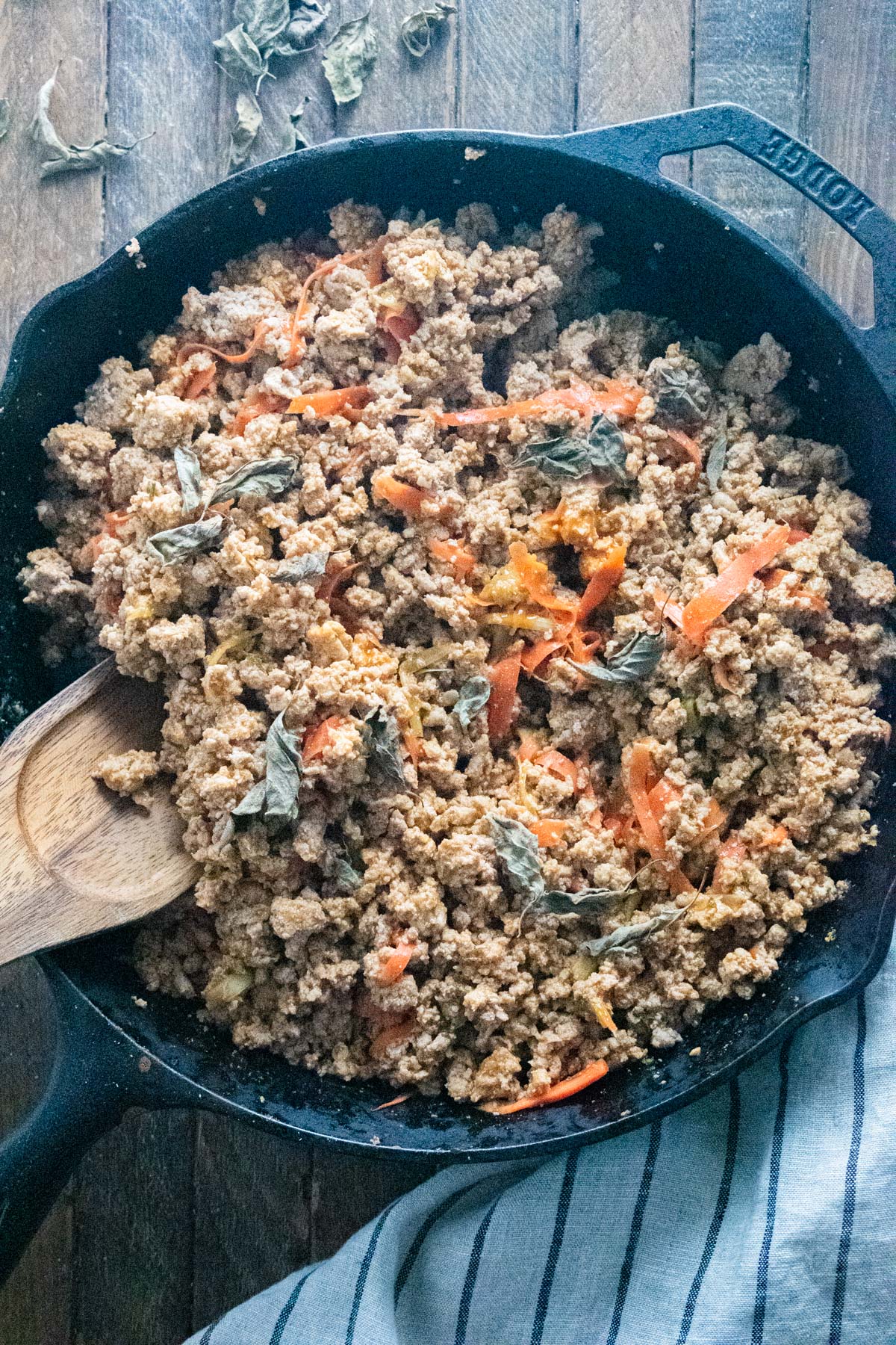 Ground turkey in a skillet with buffalo sauce and seasonings on top sitting on a wooden table.