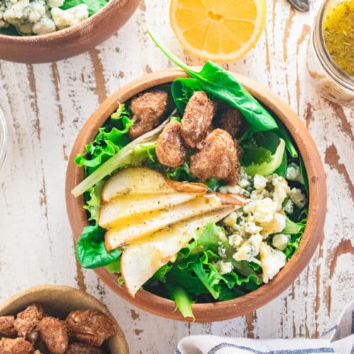 Birds eye view of a salad in a wooden bowl with sliced pears on top, gorgonzola cheese, and candied pecans.