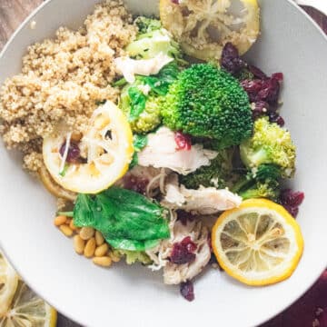 Birds-eye view of a white bowl with quinoa, chicken, broccoli, and lemon slices in it.
