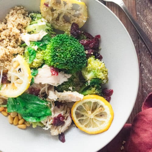 close up of juicy chicken quinoa bowl in a white bowl on a wooden table.