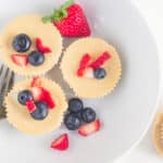 A birds-eye view of cheesecake muffins on a white plate with blueberries and strawberries.