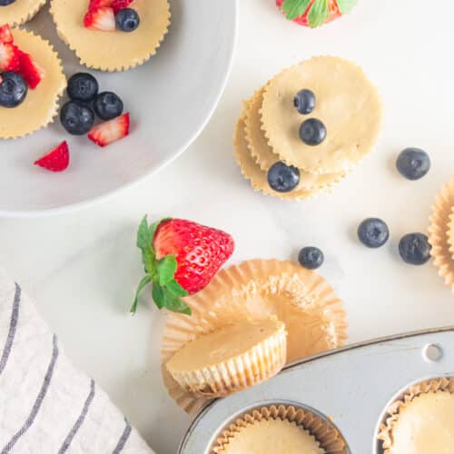 A birds eye view of cheesecake muffins on a white table with scattered blueberries and strawberries.